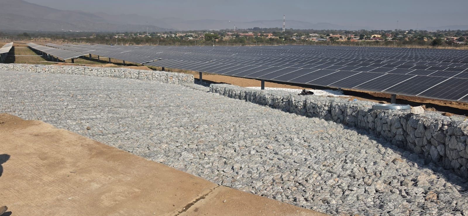 Long gabion apron of rock-filled baskets beside rows of solar panels at Balfour